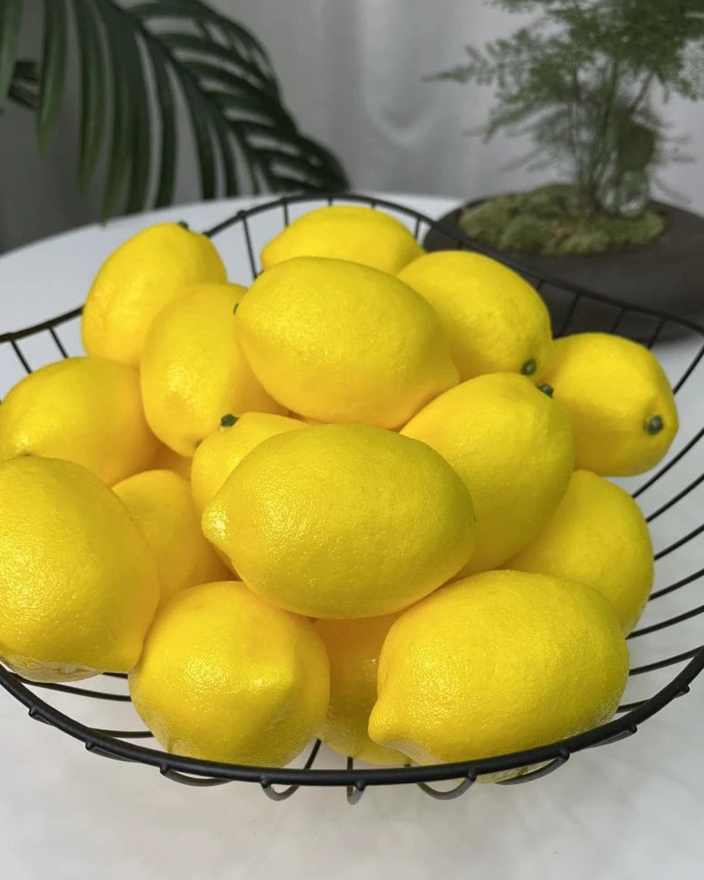 Artificial lemons in a black wire bowl on a table