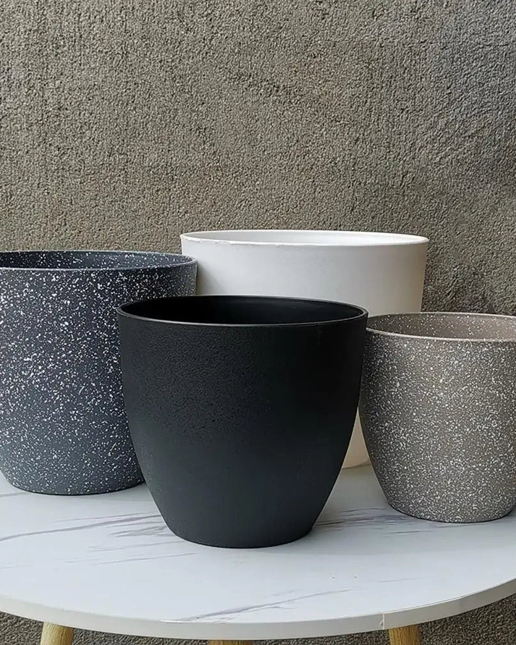 Four stone effect plant pots on a table against a concrete wall; plants not included