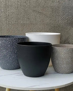 Four stone effect plant pots on a table against a concrete wall; plants not included
