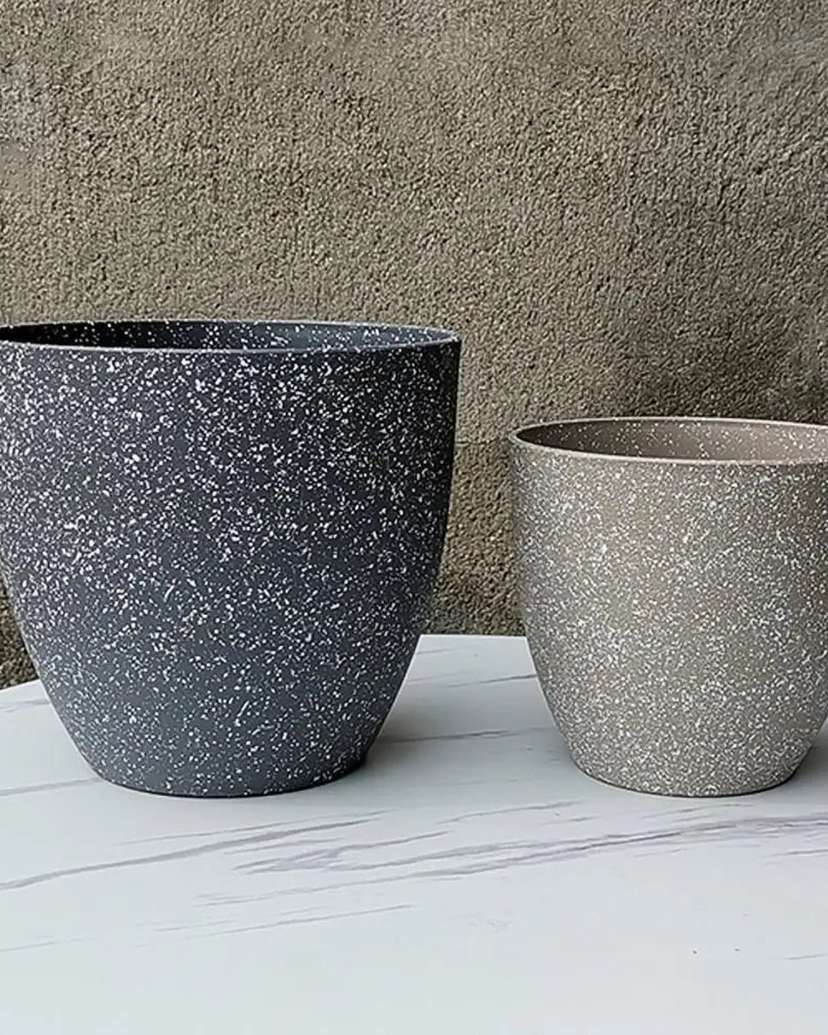 Two stone effect plant pots on marble against a concrete wall; plants not included