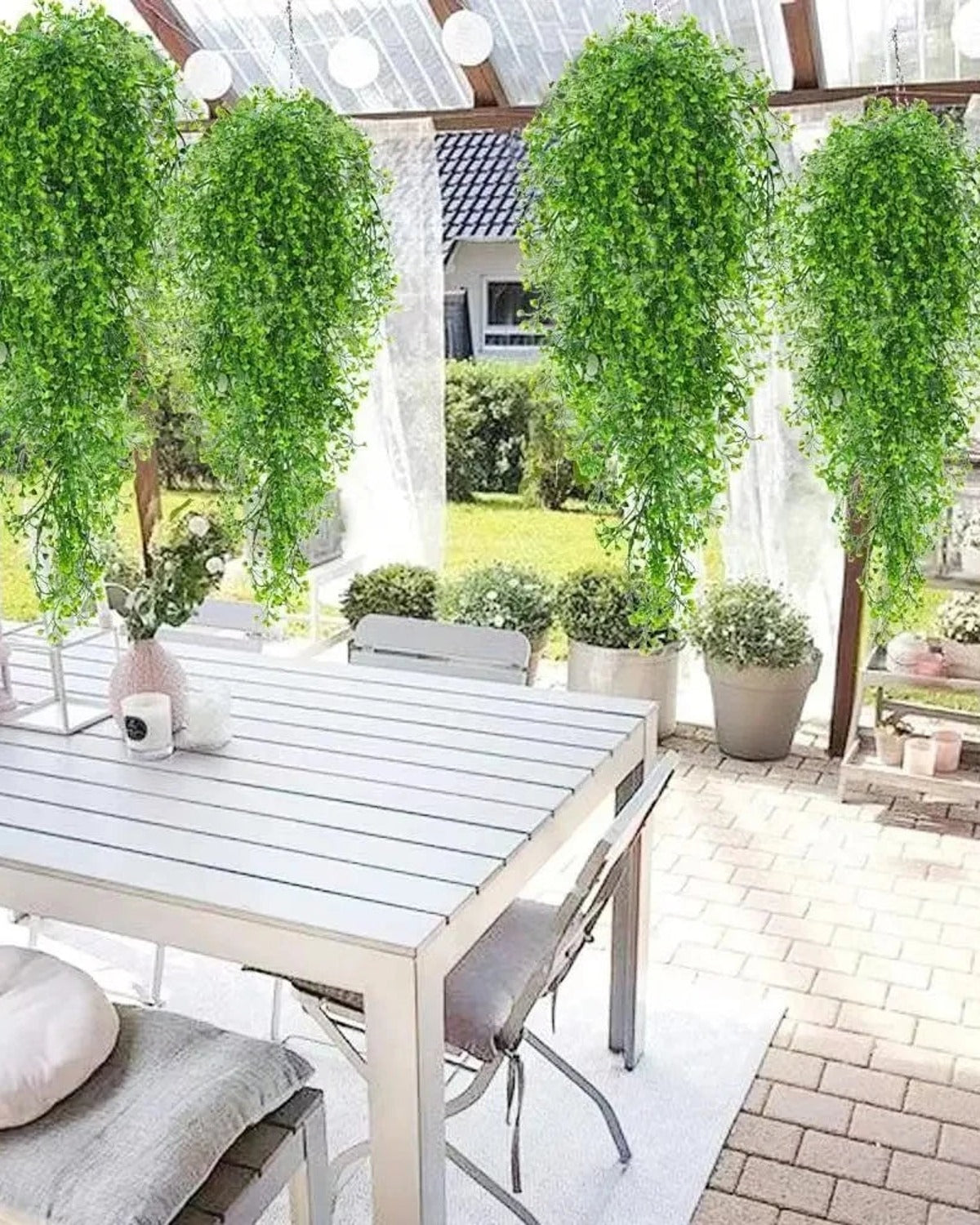 Green artificial wisteria sprays hung in a row from a pergola over a garden table; each order is one spray