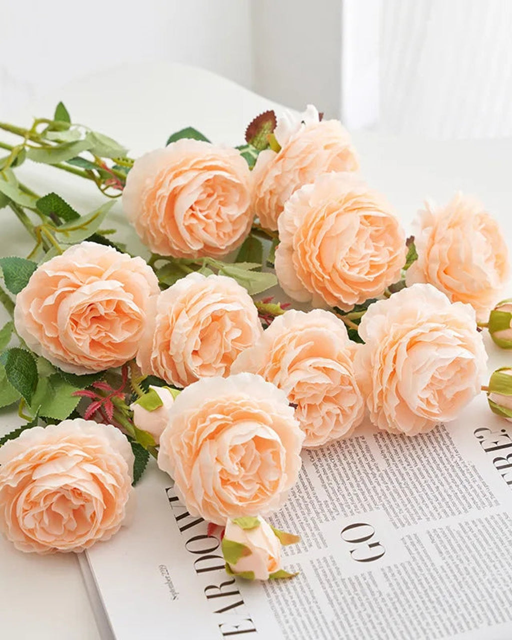 Champagne artificial rose branches laid on an open book; each order is one branch