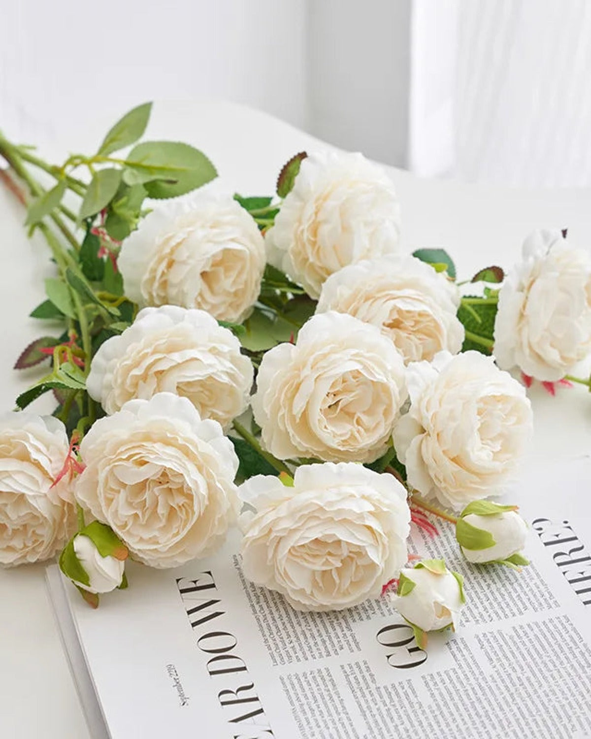 Milky white artificial rose branches laid on an open book; each order is one branch