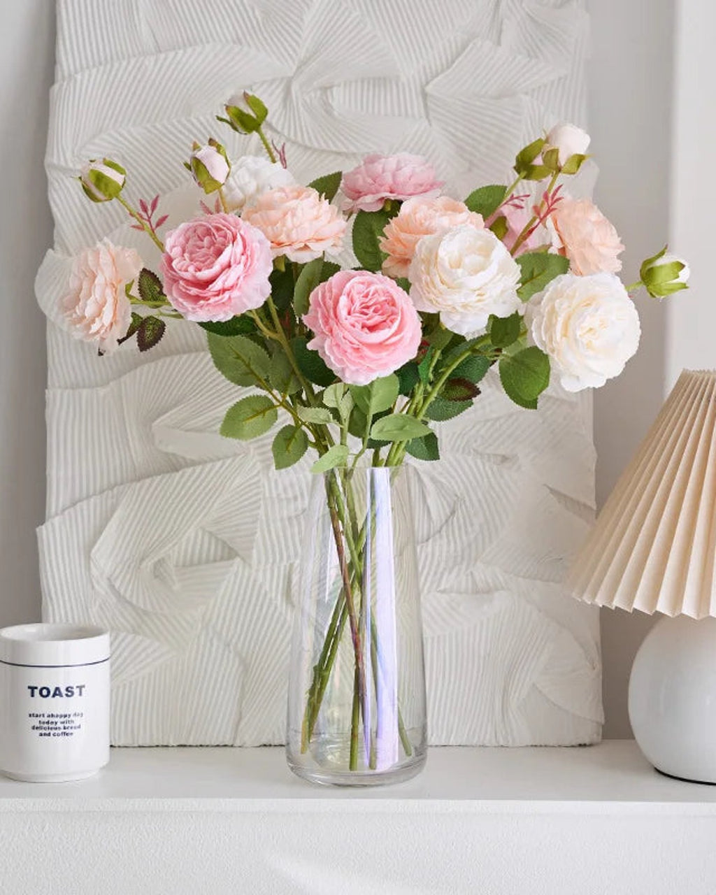 Artificial rose branches in a glass vase on a shelf beside a lamp; each order is one branch, and no vase is included