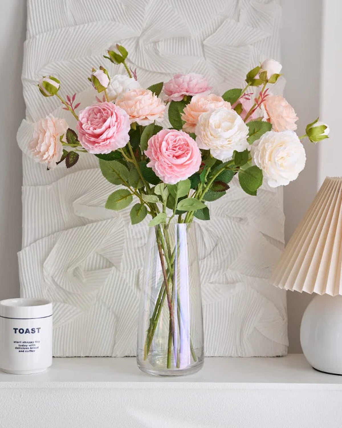 Artificial rose branches in a glass vase on a shelf beside a lamp; each order is one branch, and no vase is included