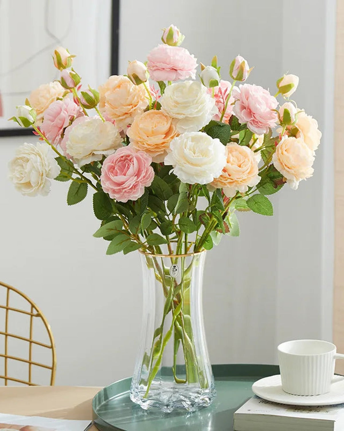 Artificial rose branches in a glass vase on a table beside a cup; each order is one branch, and no vase is included