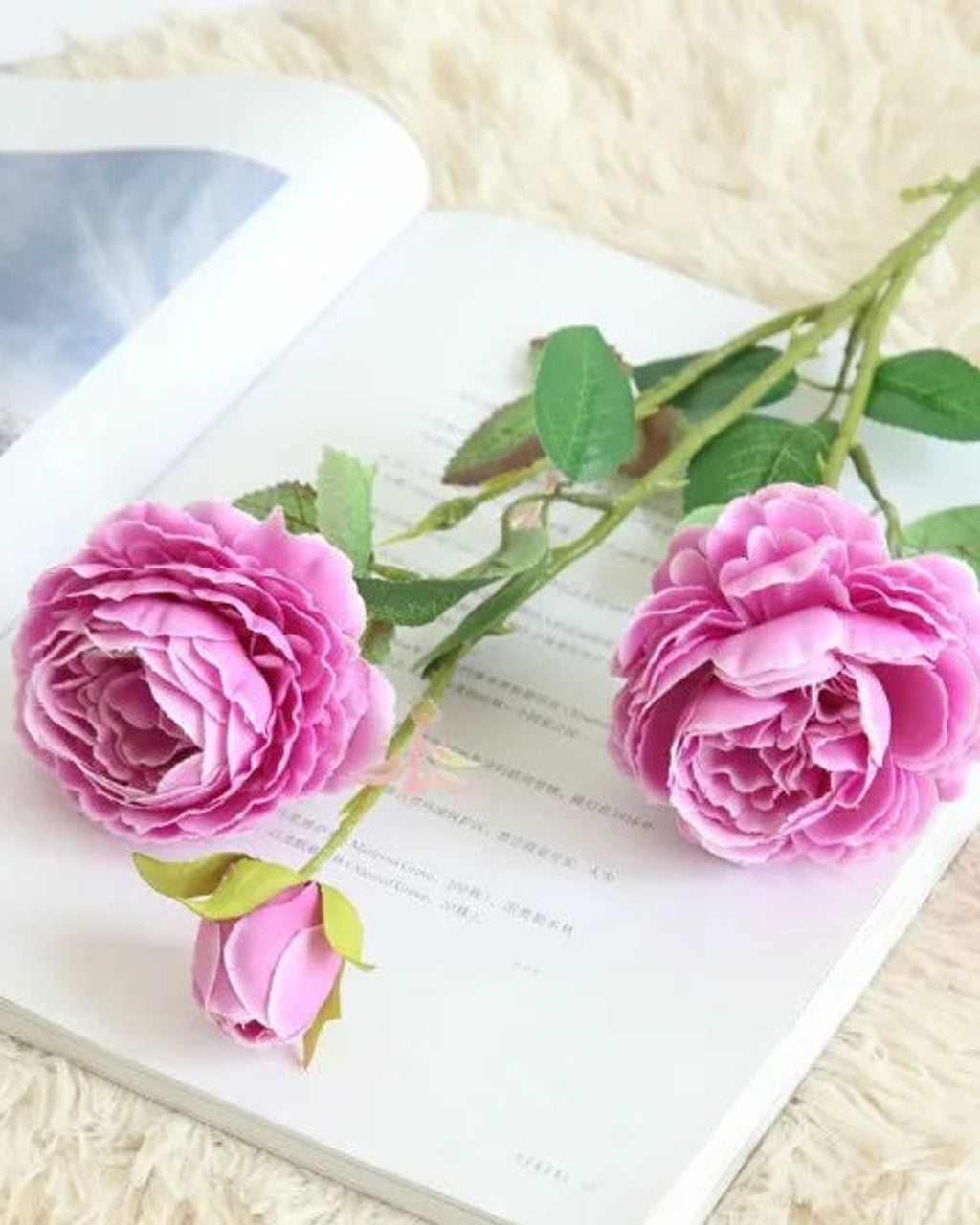 Purple, artificial rose branch: two open blooms and a bud on one stem