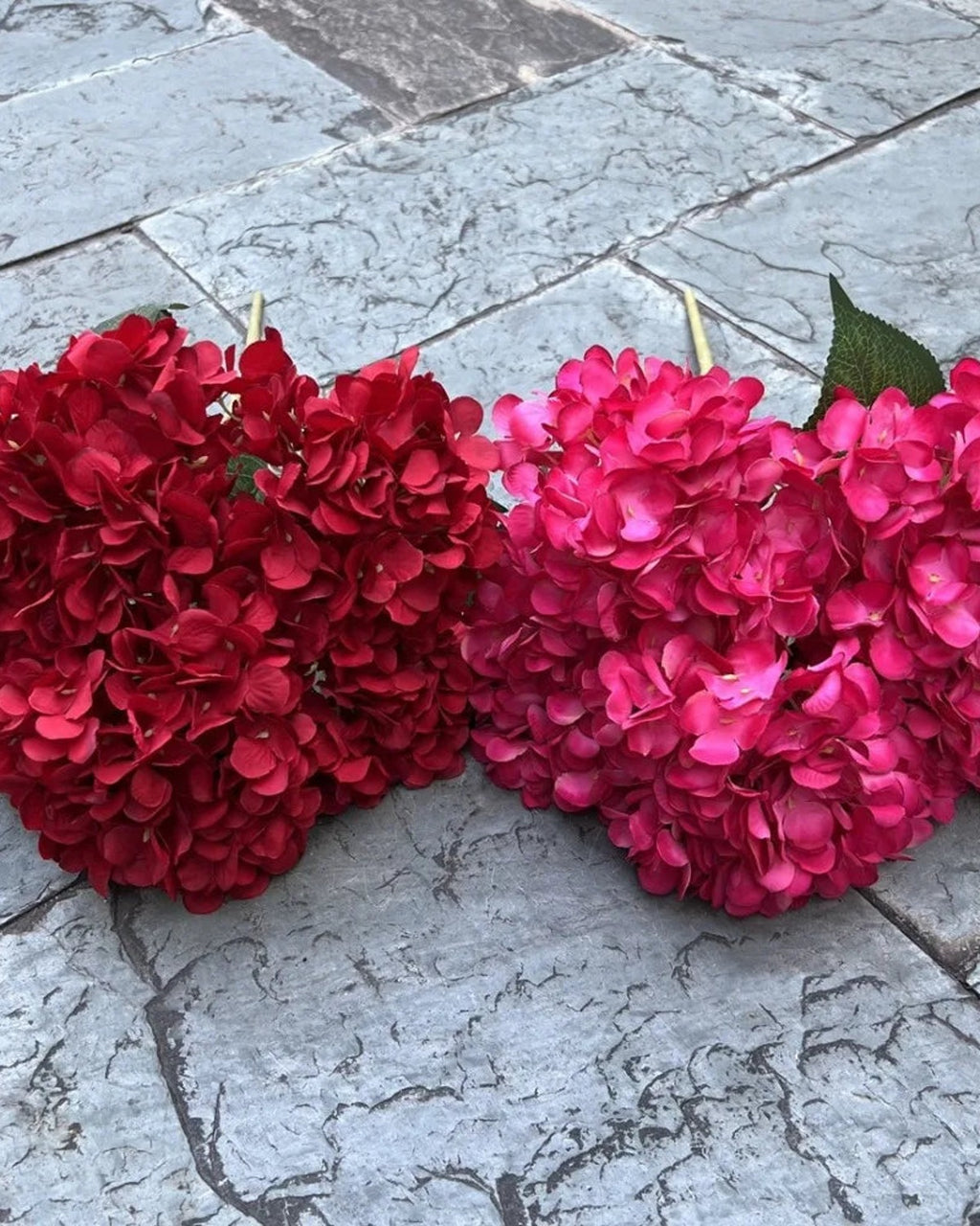 Two artificial hydrangea bunches side by side on paving, rose red and pink; each order is one bunch