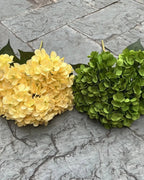 Two artificial hydrangea bunches side by side on paving, yellow and green; each order is one bunch