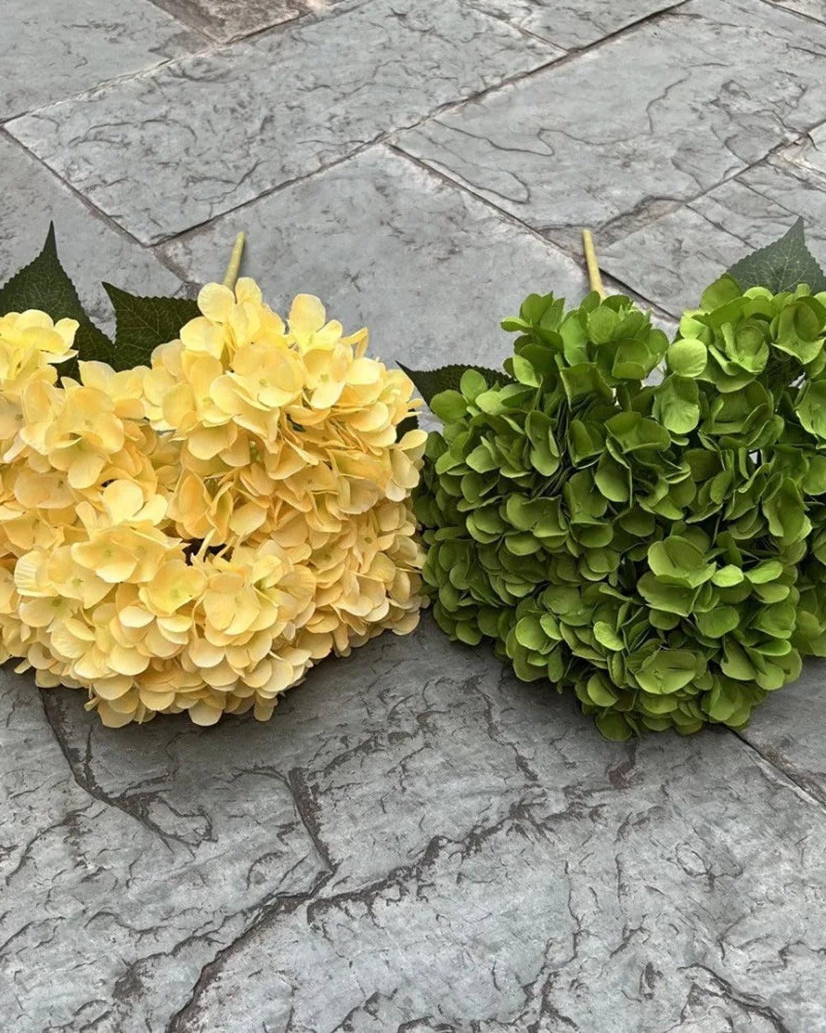 Two artificial hydrangea bunches side by side on paving, yellow and green; each order is one bunch