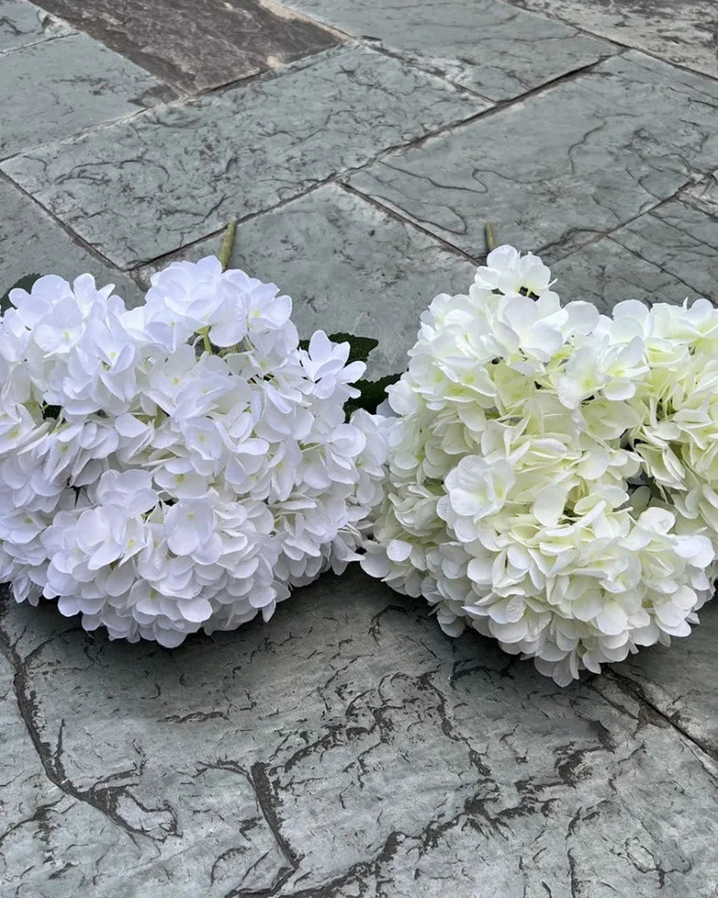 Two artificial hydrangea bunches side by side on paving, both in whites; each order is one bunch