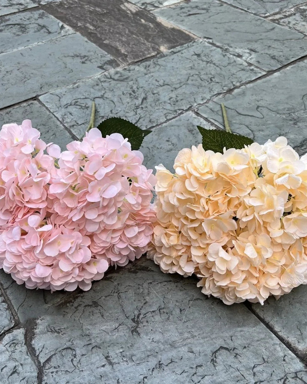 Two artificial hydrangea bunches side by side on paving, pink and champagne; each order is one bunch
