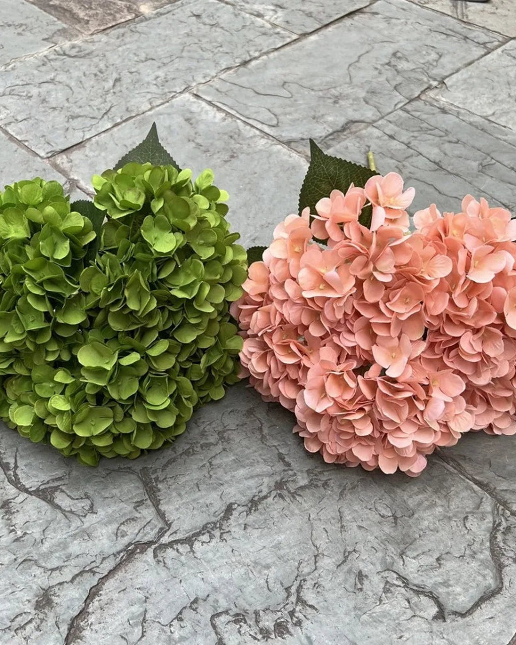 Two artificial hydrangea bunches side by side on paving, green and a paler shade; each order is one bunch