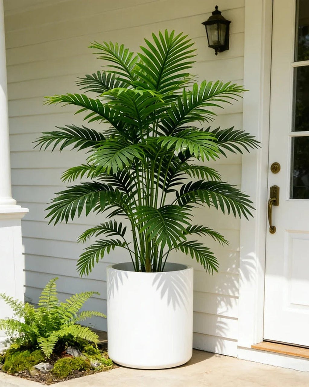 An artificial palm leaf bush beside a front door on a porch; pot not included