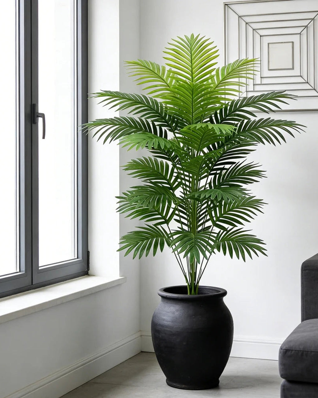 An artificial palm leaf bush beside a window in a bright room; pot not included