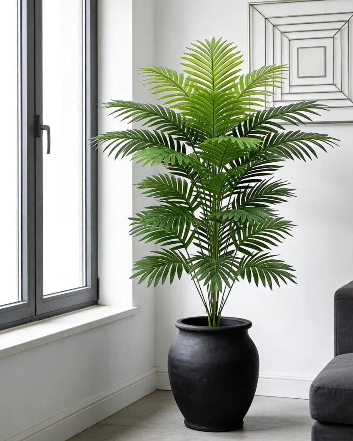 An artificial palm leaf bush beside a window in a bright room; pot not included