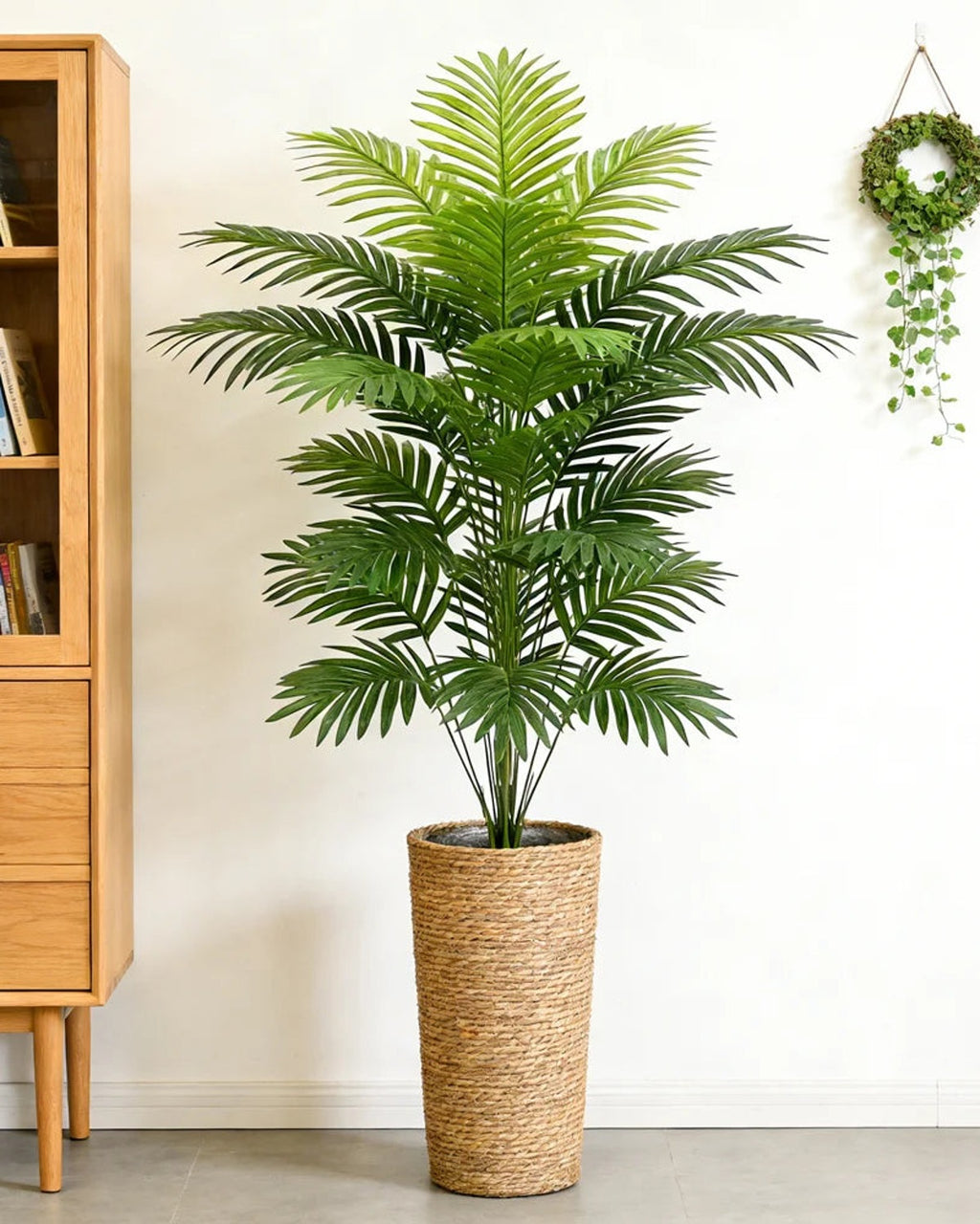 An artificial palm leaf bush beside a wooden cabinet in a hallway; pot not included