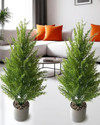 Two artificial pine trees in pots either side of a sofa in a living room; pot not included