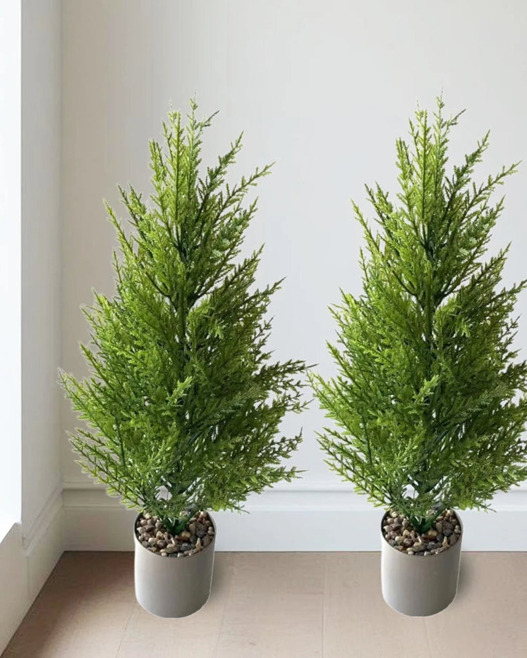 Two artificial pine trees in pots against a hallway wall; pot not included