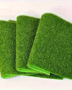 Three artificial grass mats standing on edge, showing the flexible fabric backing; each order is one mat