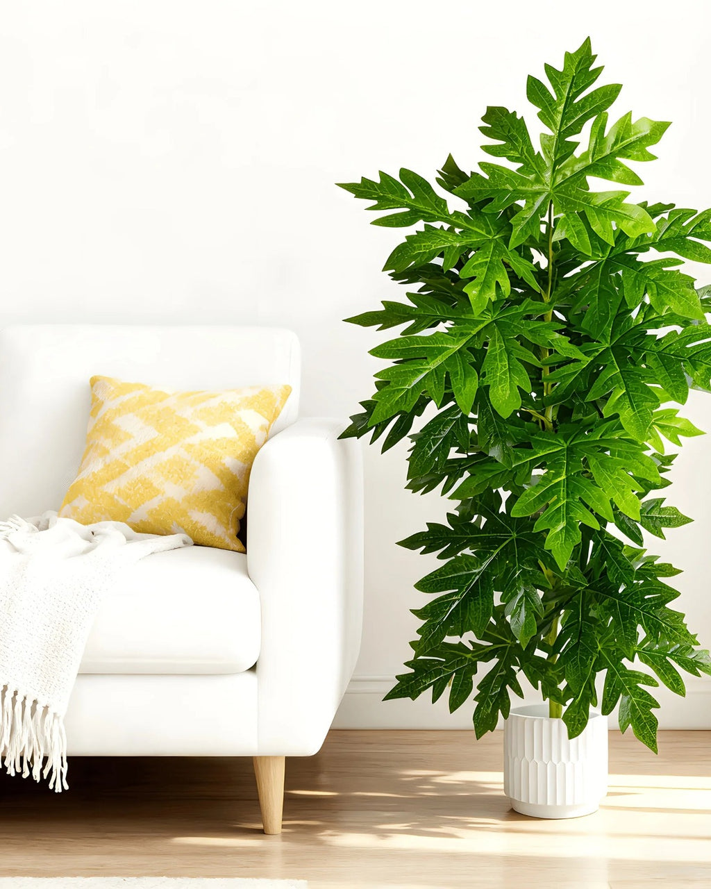 An artificial papaya leaf plant beside a cream sofa in a living room; pot not included