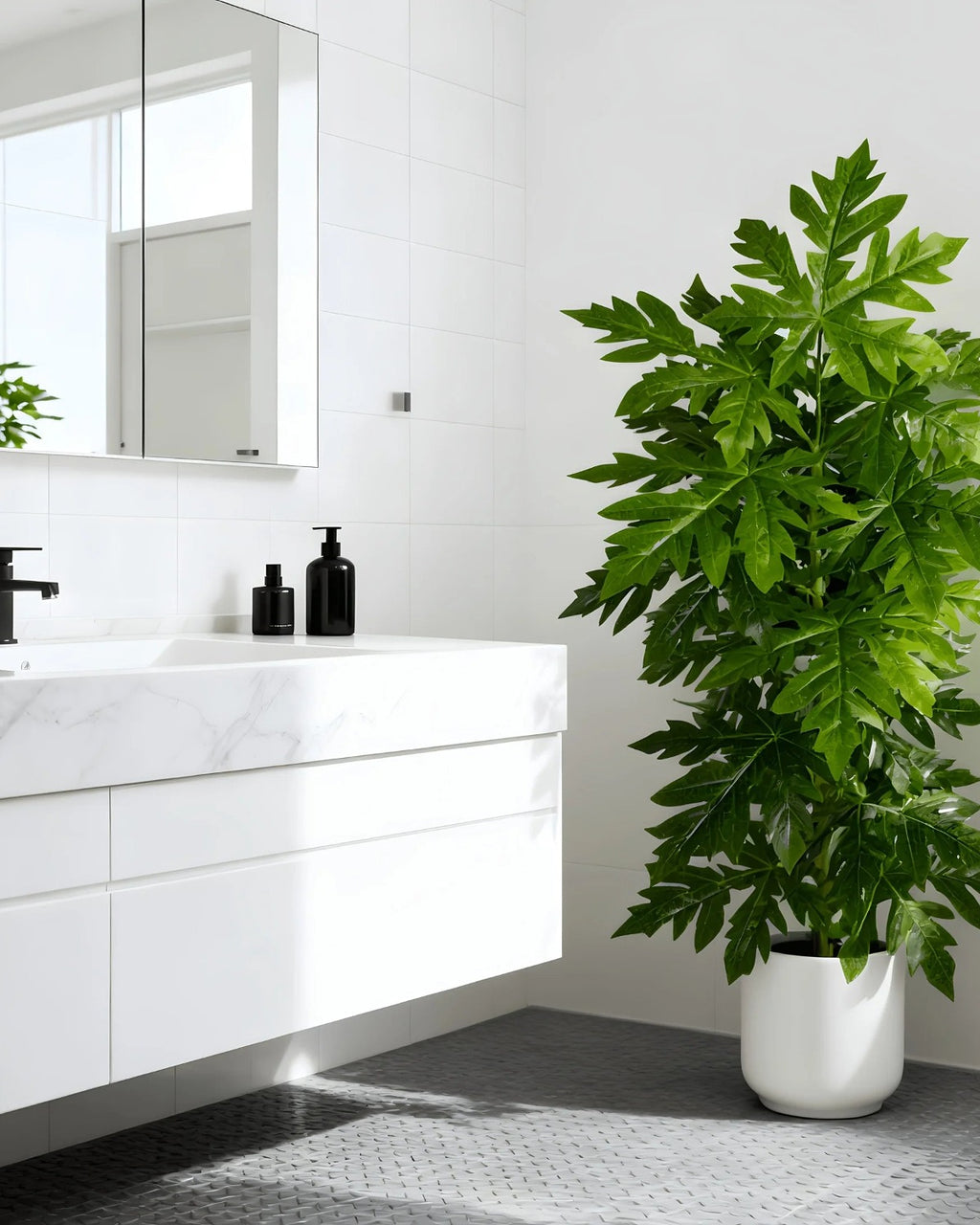 An artificial papaya leaf plant beside a basin in a white bathroom; pot not included