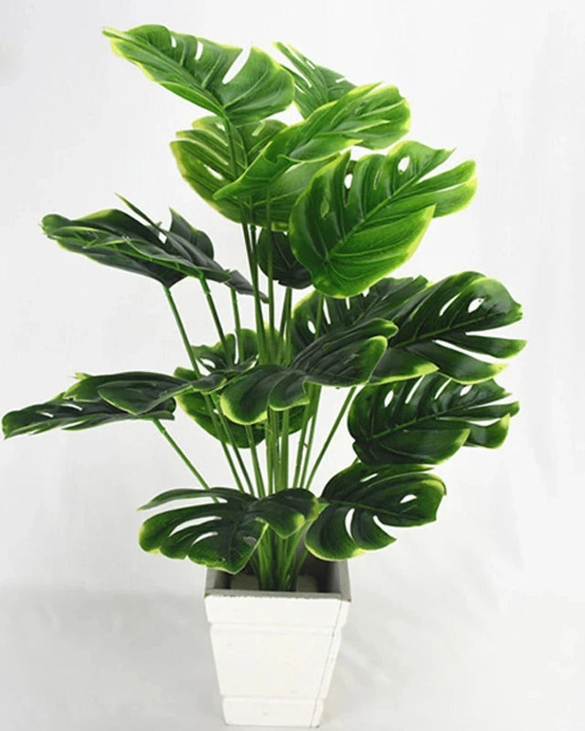 An artificial monstera plant in a plain white pot, its split leaves spread wide; pot not included
