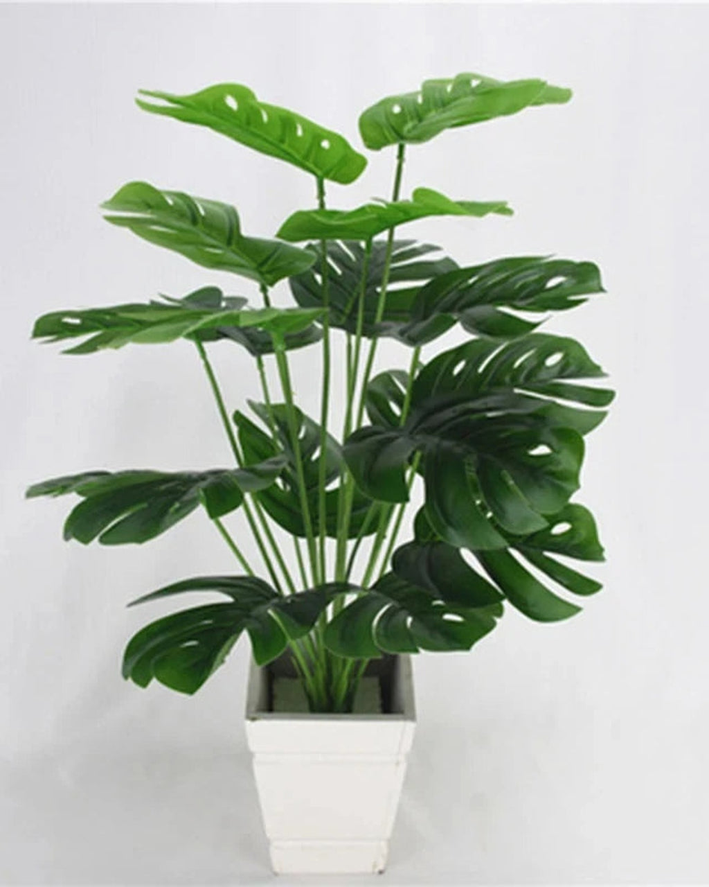 An artificial monstera plant in a plain white pot, its taller leaves standing above the rest; pot not included