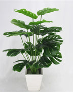 An artificial monstera plant in a plain white pot, its taller leaves standing above the rest; pot not included