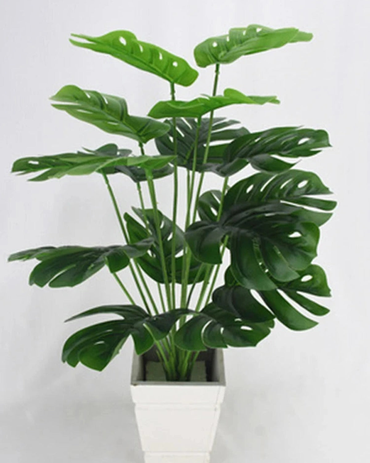 An artificial monstera plant in a plain white pot, seen slightly from the side; pot not included