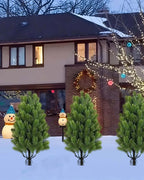 Artificial mini Christmas trees pushed into snow on their ground spikes outside a lit house; each order is two trees