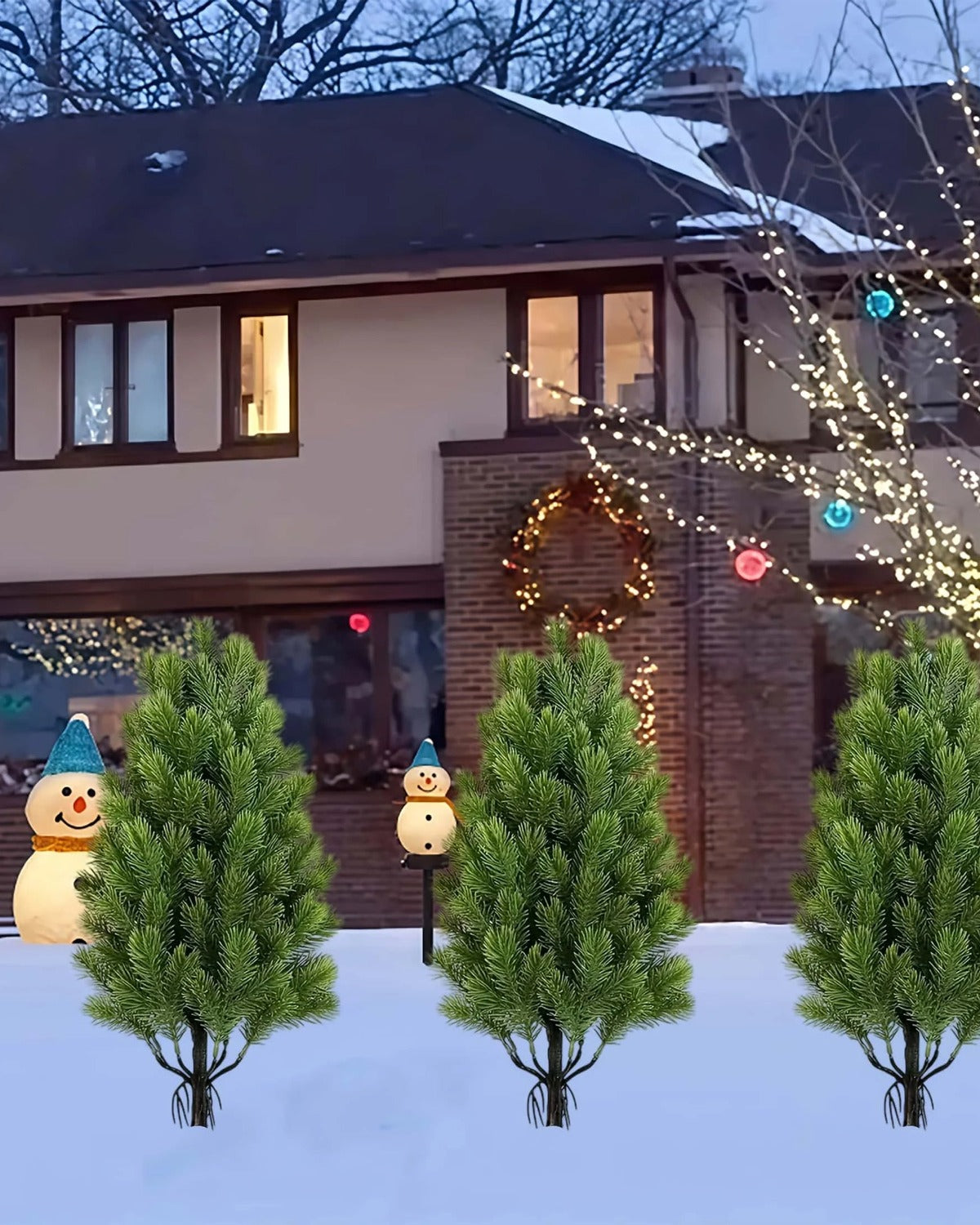 Artificial mini Christmas trees pushed into snow on their ground spikes outside a lit house; each order is two trees