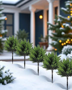 Artificial mini Christmas trees on their ground spikes lining a snowy path; each order is two trees