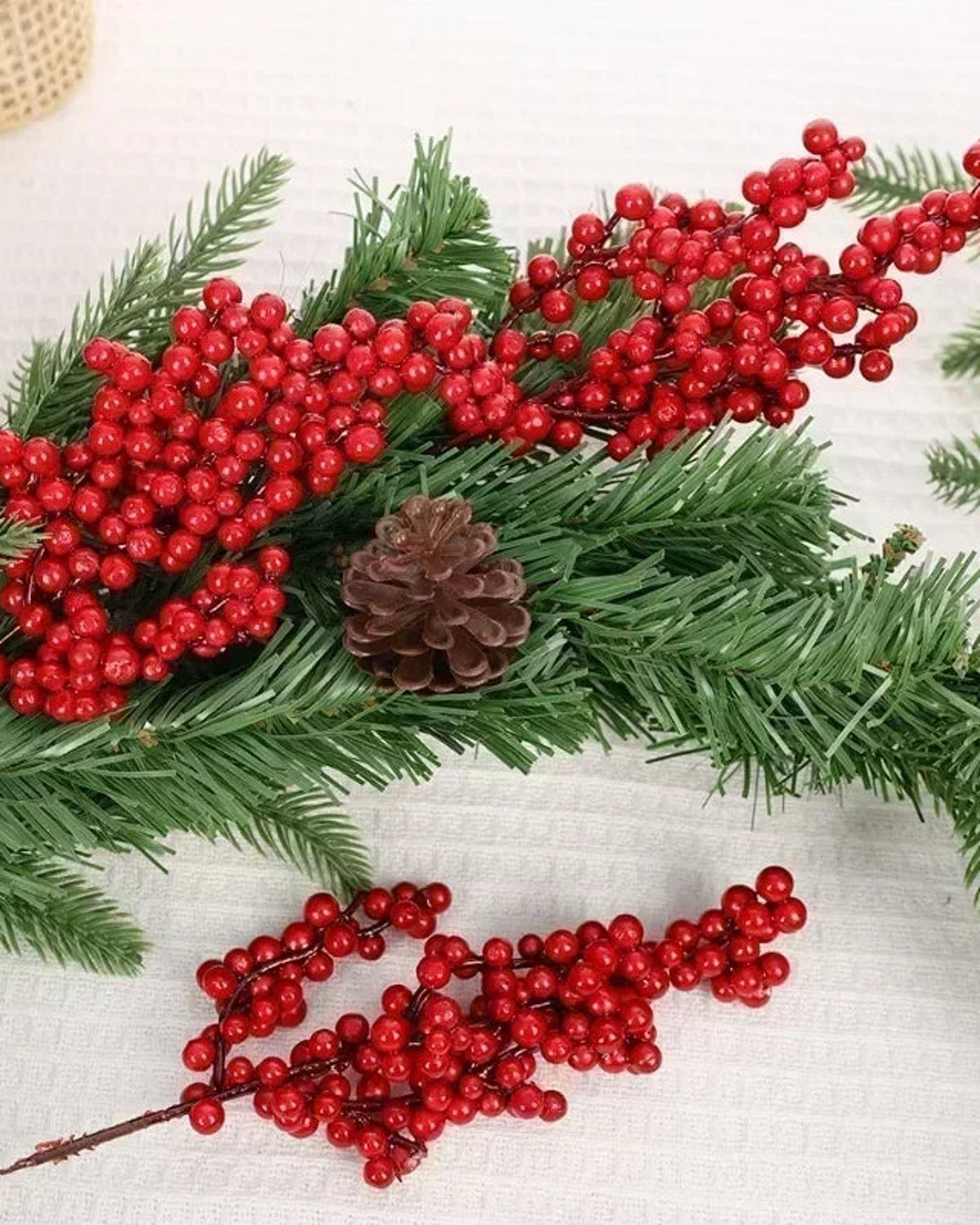 Artificial berry branches laid with pine foliage and a pine cone; only the berry branches are part of the order