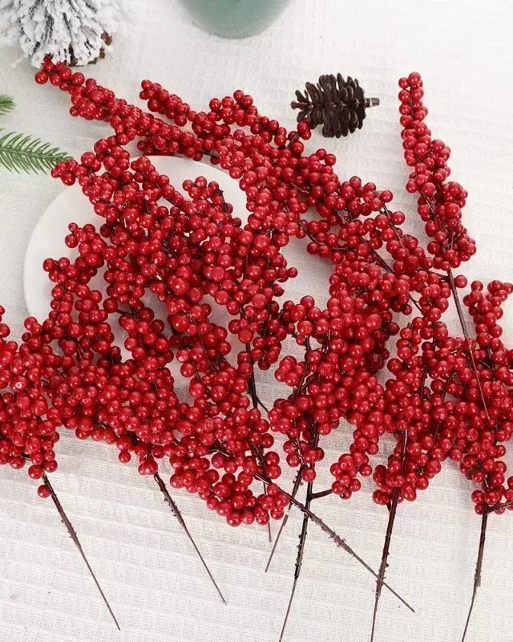 Artificial berry branches laid out on a white cloth with a pine cone; only the berry branches are part of the order