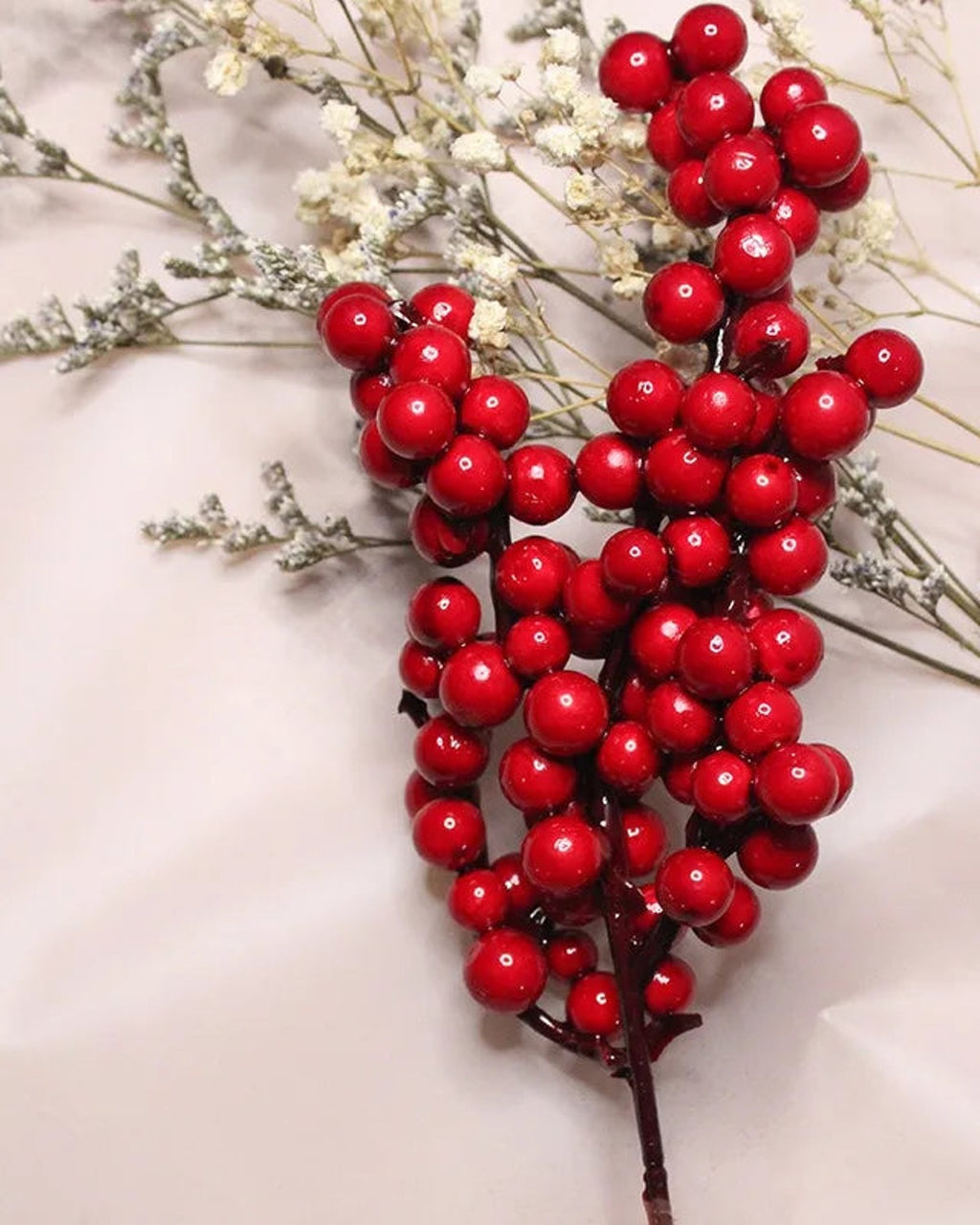 A single artificial berry branch on a pale ground, its clustered round berries in close view