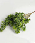A single artificial pine branch laid flat on a pale background