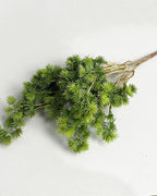 A single artificial pine branch laid flat on a pale background
