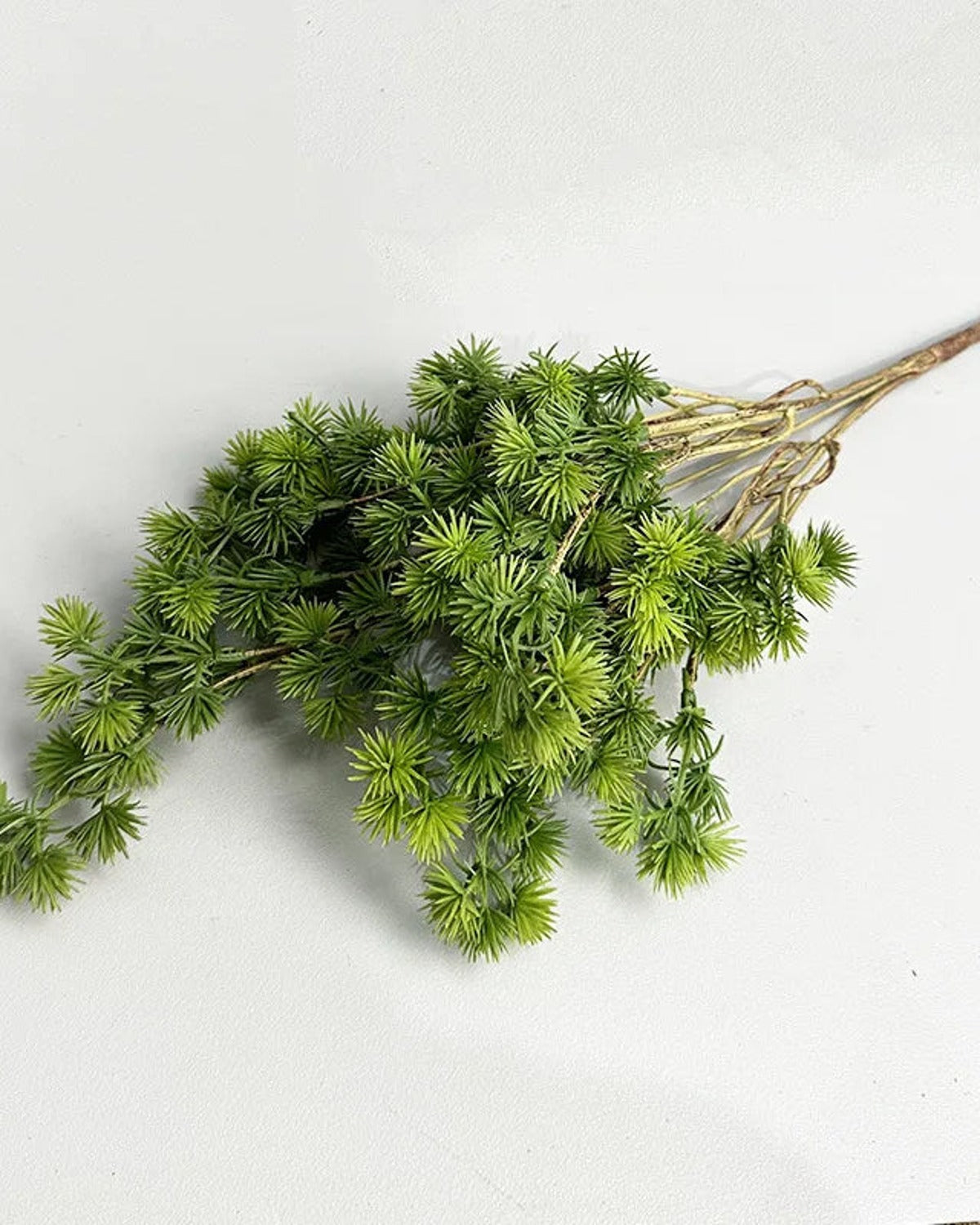 A single artificial pine branch laid flat, its cut end to the right