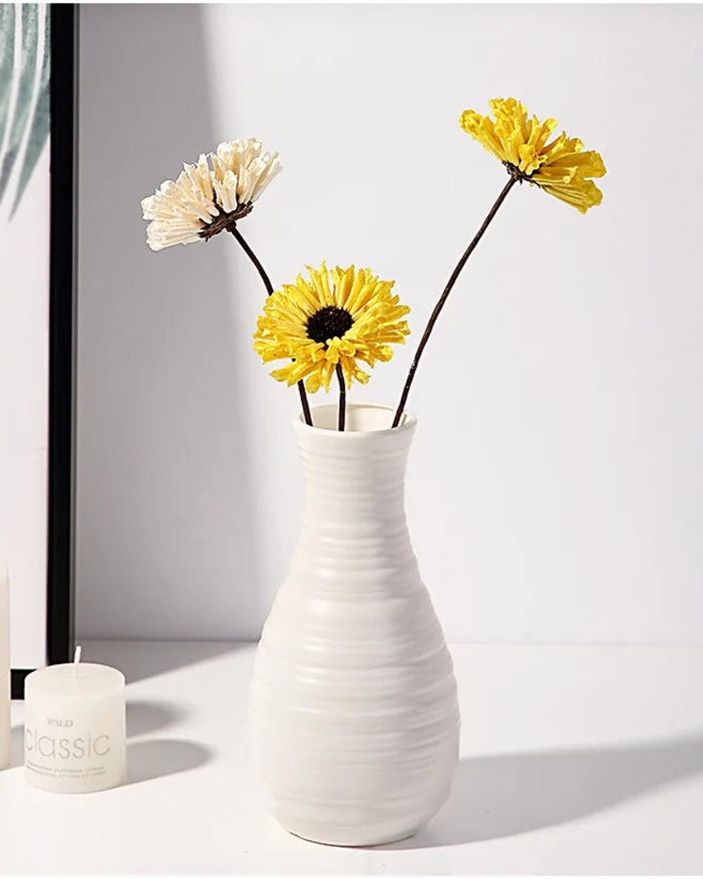 A fluted white origami vase holding dried flowers beside a candle; flowers not included