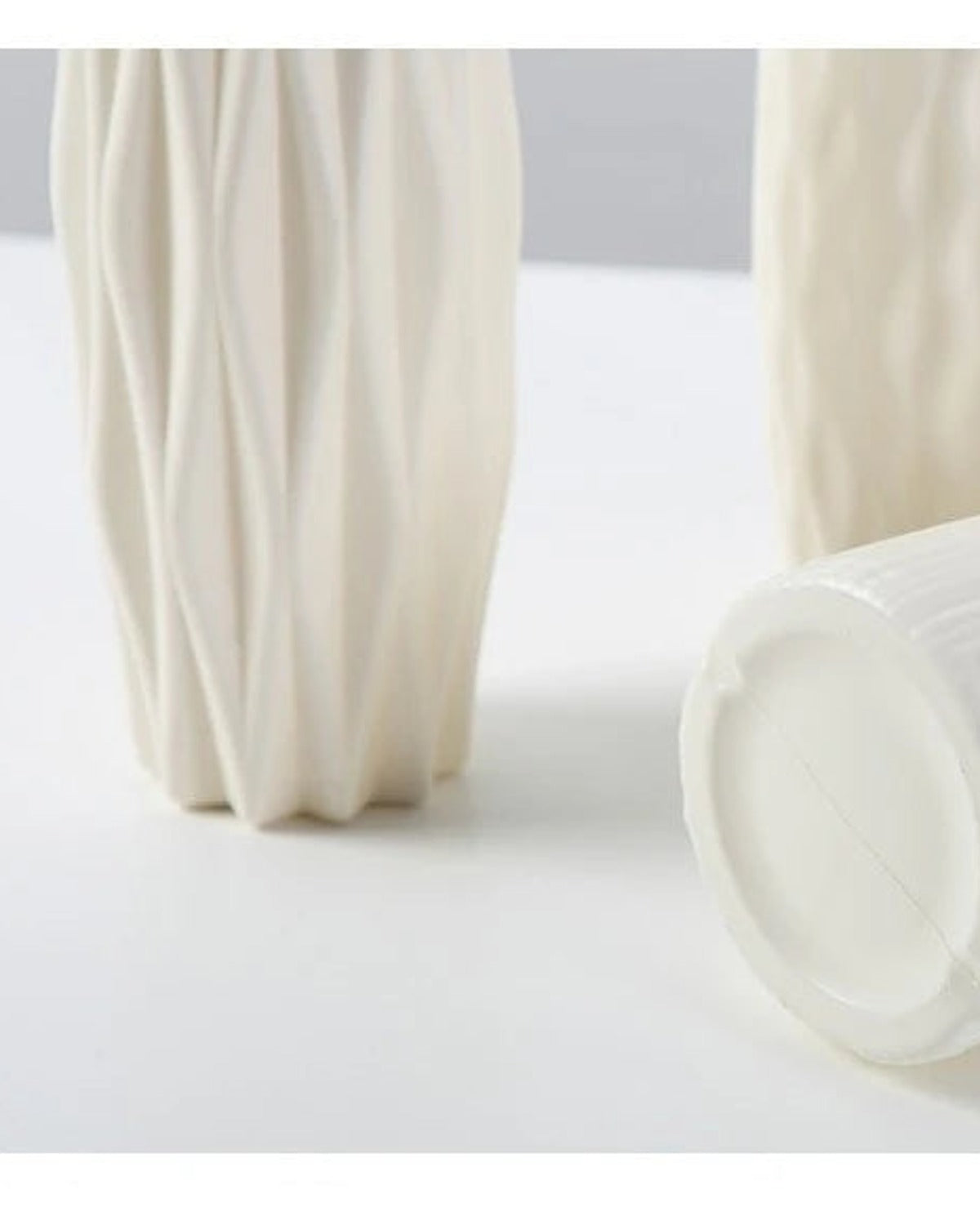 Two white origami vases, one on its side, showing the mouth and the wall thickness