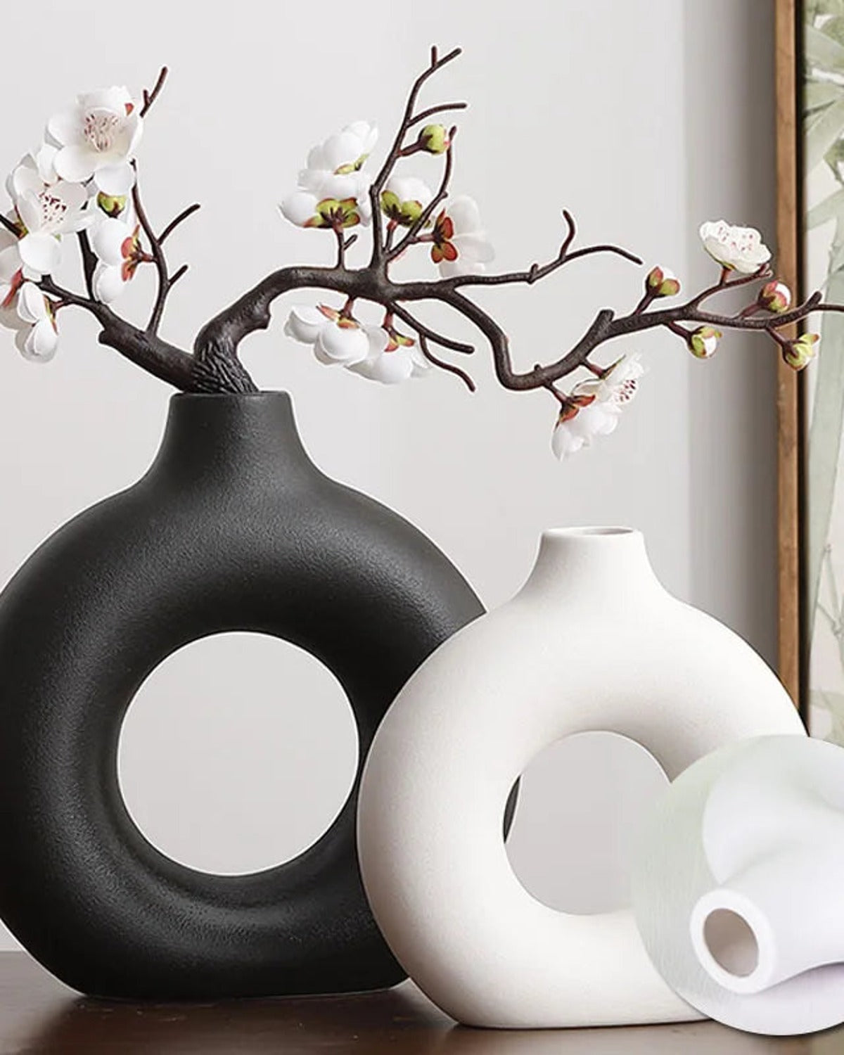 A black donut vase and two white ones with a blossom branch; flowers not included