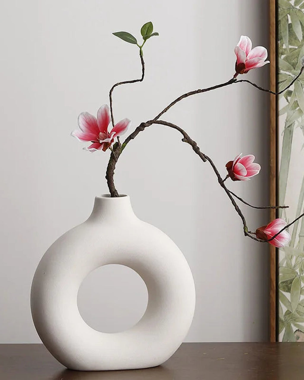 A white donut vase holding a magnolia branch; flowers not included