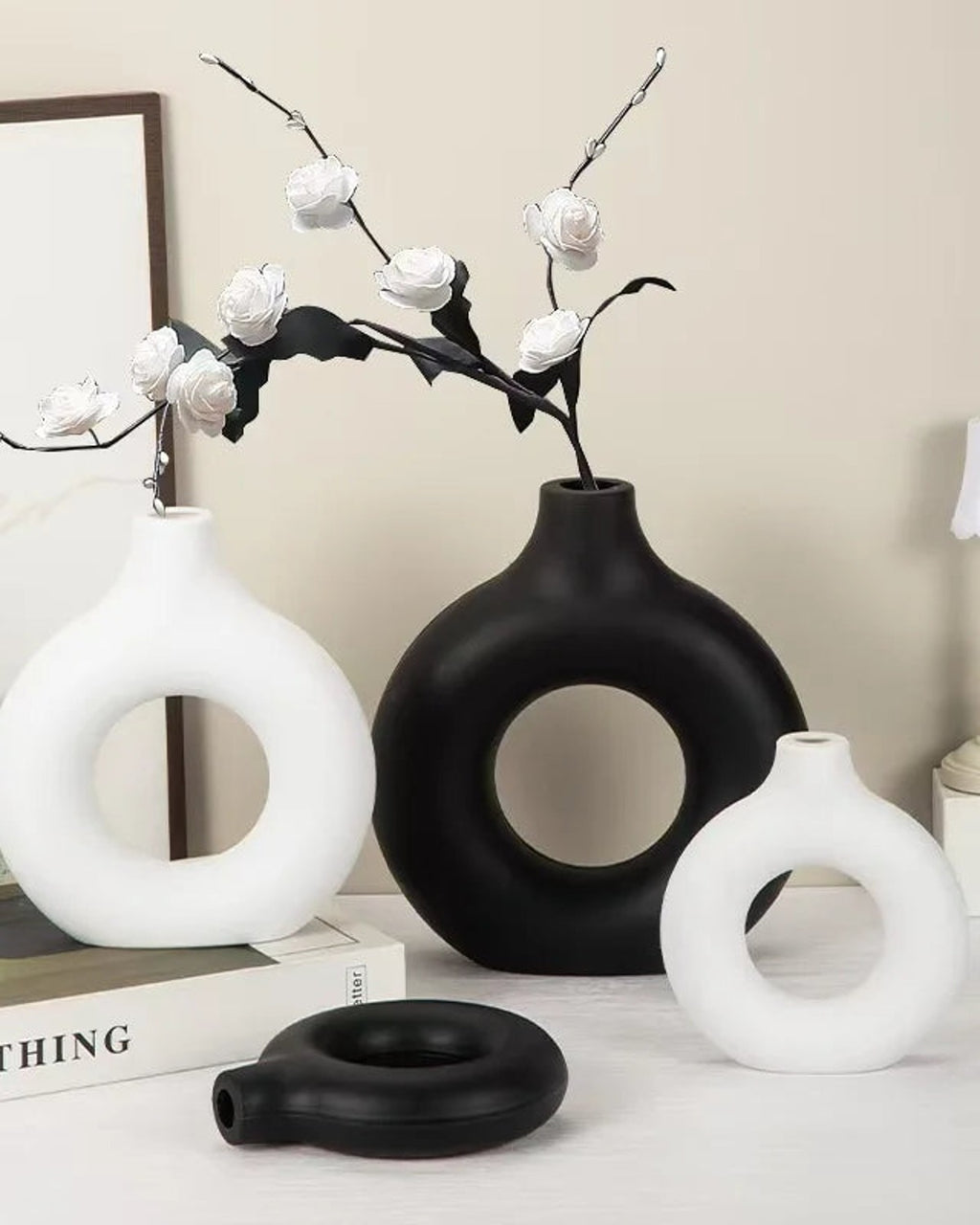 White and black donut vases with blossom branches on a console; flowers not included
