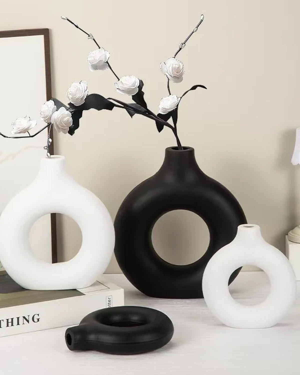 White and black donut vases with blossom branches on a console; flowers not included