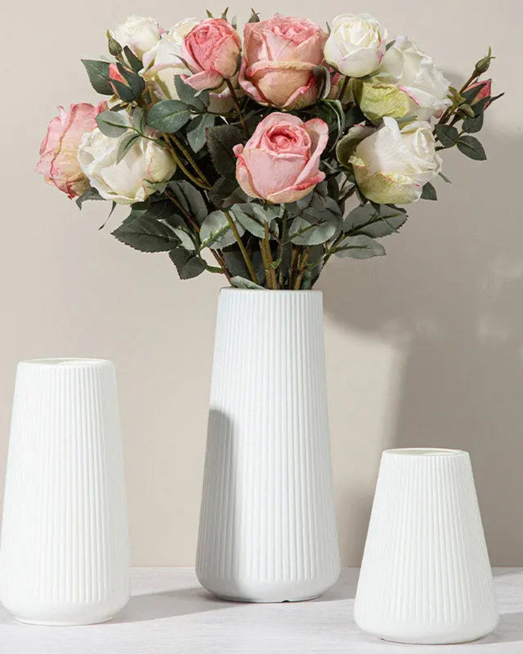 A fluted tapered vase holding garden roses beside two empty ones; flowers not included