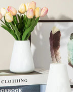 A fluted tapered vase holding tulips beside an empty one; flowers and feathers not included