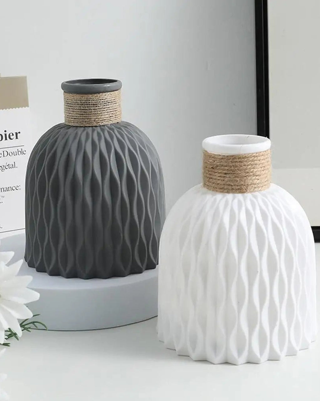A dark gray and a white rope neck vase side by side with a daisy; flowers not included