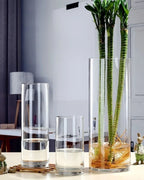 Three clear acrylic cylinder vases on a sideboard holding bamboo and reeds; stems not included