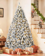A pre-lit snow flocked Christmas tree lit at the foot of a staircase; stockings, garland and gifts not included